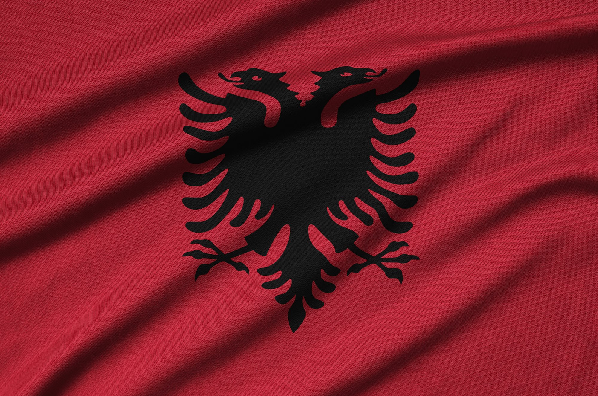 Albania flag is depicted on a sports cloth fabric with many folds. Sport team waving banner